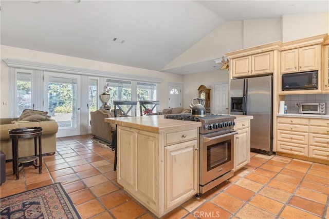 kitchen with light tile patterned flooring, high vaulted ceiling, decorative backsplash, stainless steel appliances, and cream cabinetry