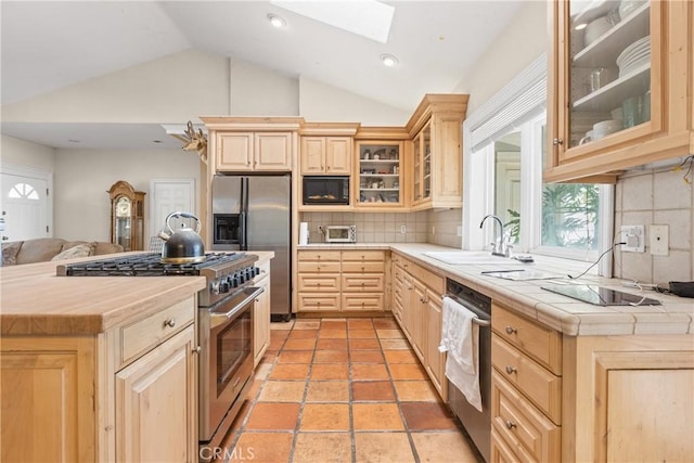 kitchen featuring light brown cabinetry, lofted ceiling with skylight, tile countertops, and stainless steel appliances