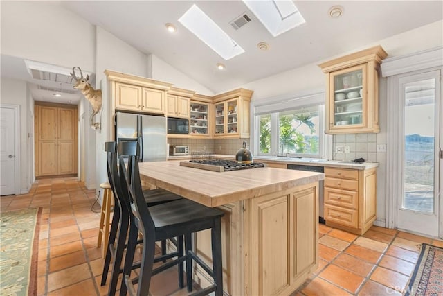 kitchen with lofted ceiling with skylight, a kitchen island, wood counters, dishwasher, and stainless steel gas cooktop