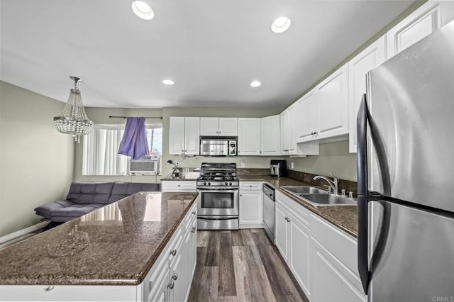 kitchen with appliances with stainless steel finishes, sink, white cabinets, hanging light fixtures, and dark wood-type flooring