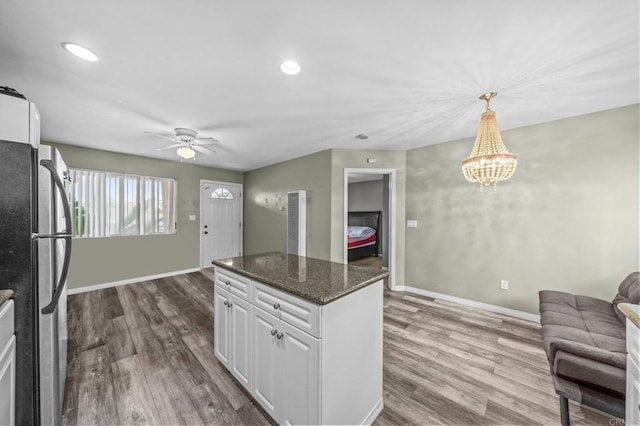 kitchen featuring stainless steel refrigerator, hanging light fixtures, wood-type flooring, white cabinets, and dark stone counters