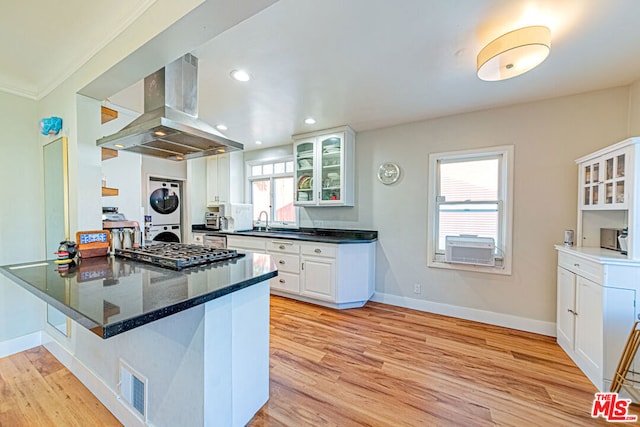 kitchen with stacked washer and dryer, white cabinets, island exhaust hood, kitchen peninsula, and stainless steel gas stovetop