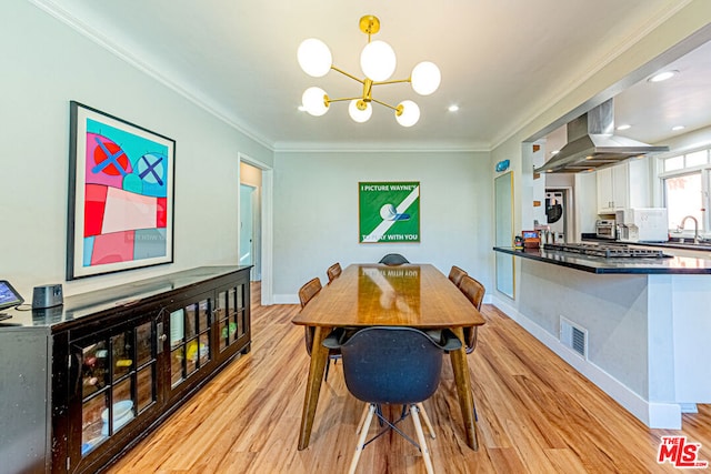 dining room with sink, a notable chandelier, light hardwood / wood-style flooring, and ornamental molding