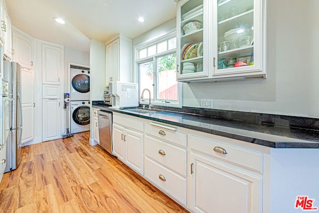 kitchen with white cabinetry, stainless steel dishwasher, stacked washer and clothes dryer, and sink