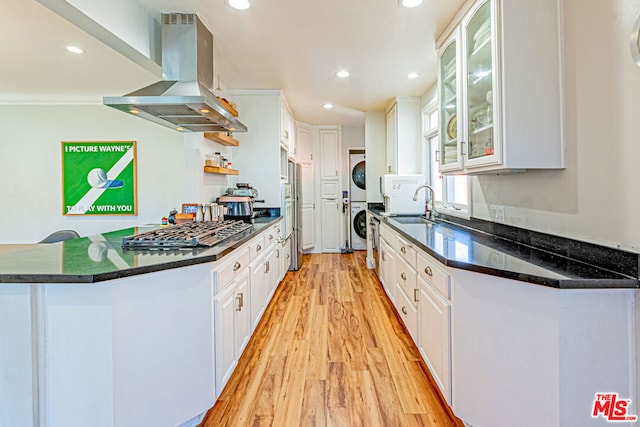 kitchen with sink, island range hood, stainless steel gas stovetop, stacked washing maching and dryer, and white cabinets