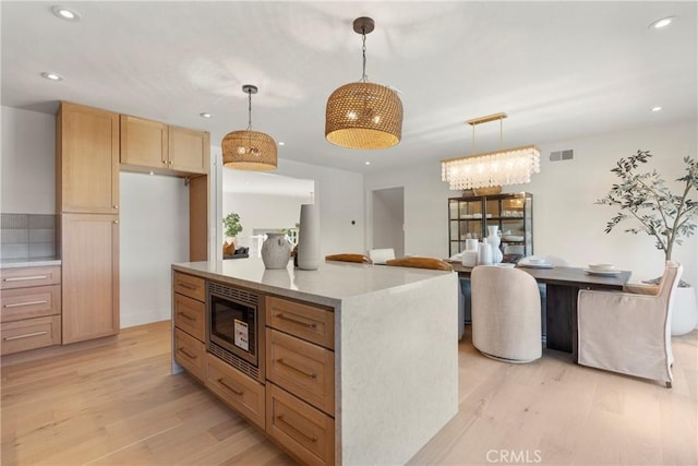 kitchen featuring pendant lighting, stainless steel microwave, light brown cabinetry, and light hardwood / wood-style floors