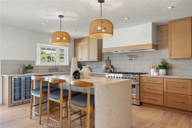 kitchen featuring wine cooler, high end stainless steel range, a center island, hanging light fixtures, and light brown cabinets