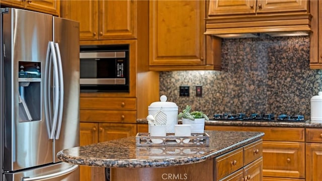 kitchen with appliances with stainless steel finishes, a center island, custom range hood, decorative backsplash, and dark stone counters