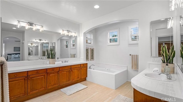 bathroom with a relaxing tiled tub, vanity, and tile patterned flooring