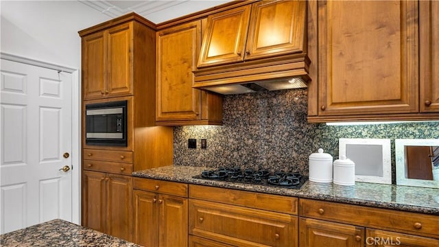 kitchen featuring stainless steel microwave, backsplash, black gas stovetop, and dark stone counters