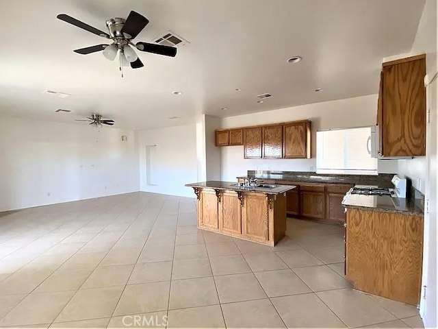 kitchen with sink, light tile patterned floors, a kitchen island, ceiling fan, and stove