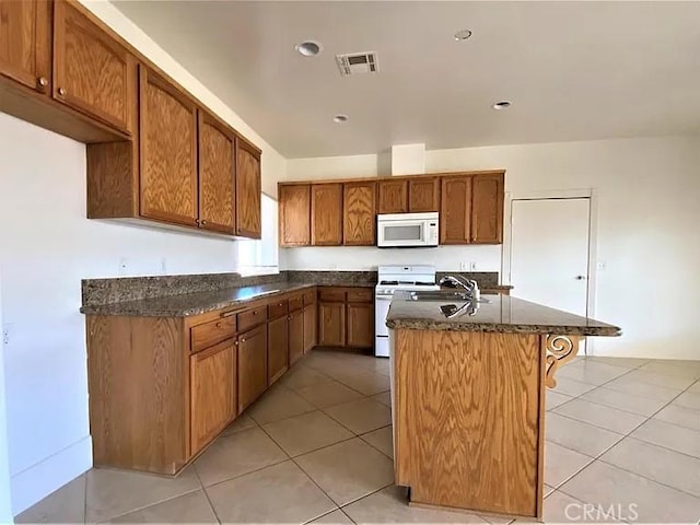 kitchen featuring sink, light tile patterned floors, white appliances, and an island with sink