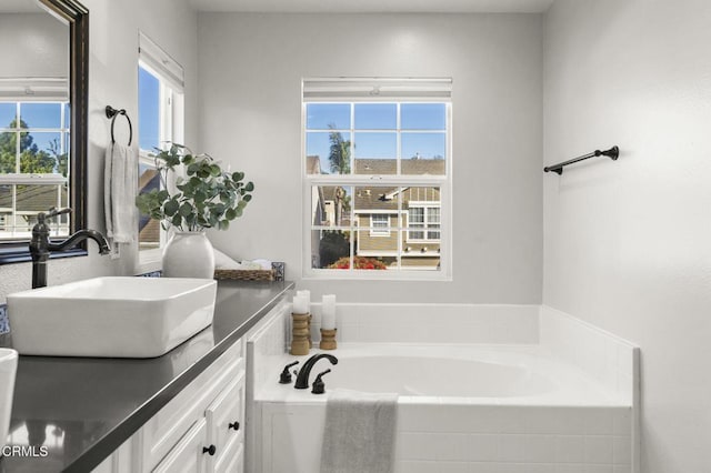 bathroom featuring plenty of natural light, vanity, and tiled tub