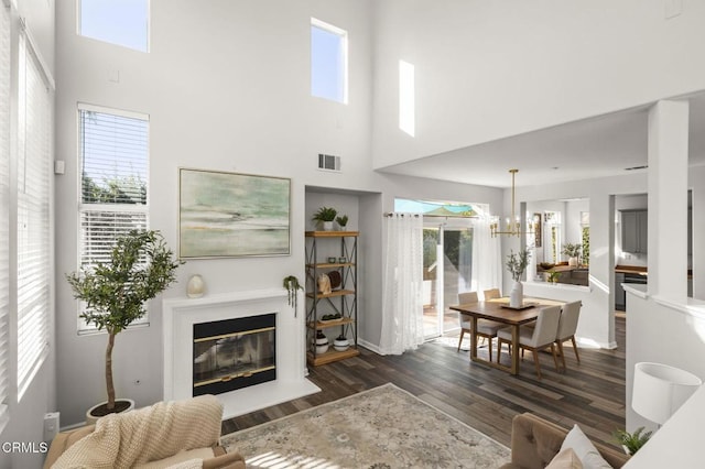 living room with a high ceiling, dark wood-type flooring, a chandelier, and plenty of natural light