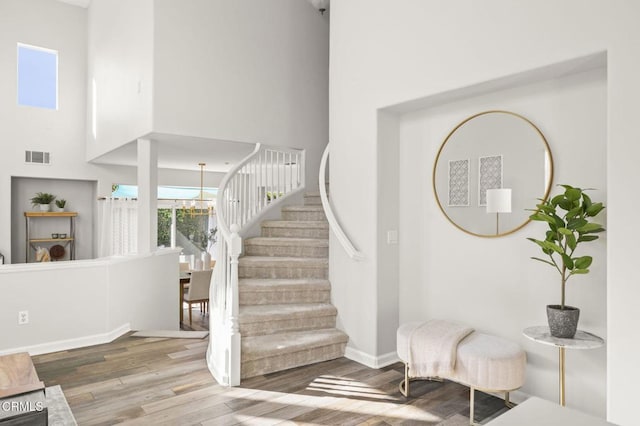 staircase with hardwood / wood-style flooring, a towering ceiling, and a chandelier