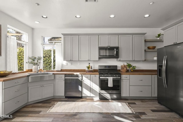 kitchen with dark wood-type flooring, sink, butcher block countertops, gray cabinets, and stainless steel appliances