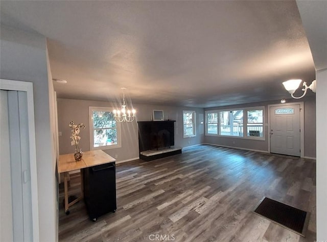 unfurnished living room featuring a notable chandelier, a wealth of natural light, and dark wood-type flooring