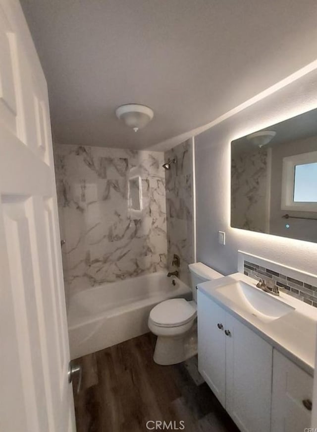 full bathroom with toilet, wood-type flooring, vanity, tiled shower / bath combo, and decorative backsplash