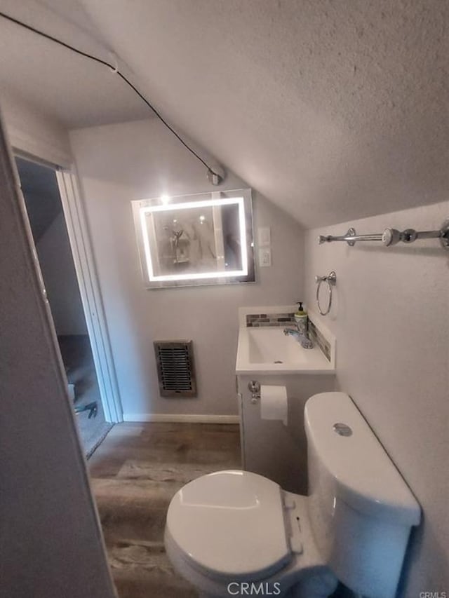 bathroom with lofted ceiling, toilet, heating unit, a textured ceiling, and vanity