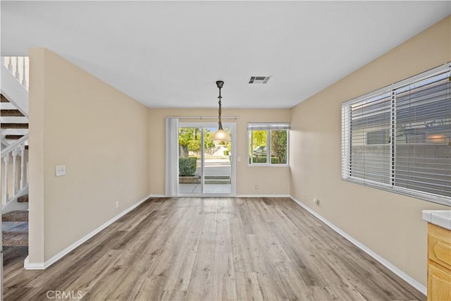unfurnished dining area featuring visible vents, baseboards, stairs, and light wood-type flooring