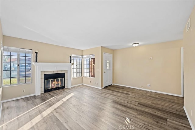 unfurnished living room featuring a tiled fireplace, visible vents, baseboards, and wood finished floors