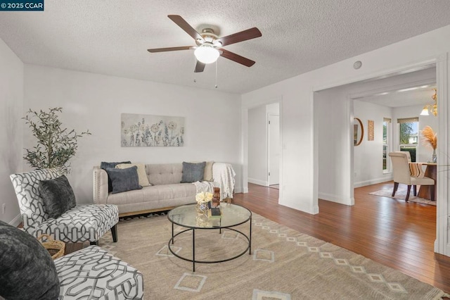 living room with hardwood / wood-style flooring, ceiling fan with notable chandelier, and a textured ceiling