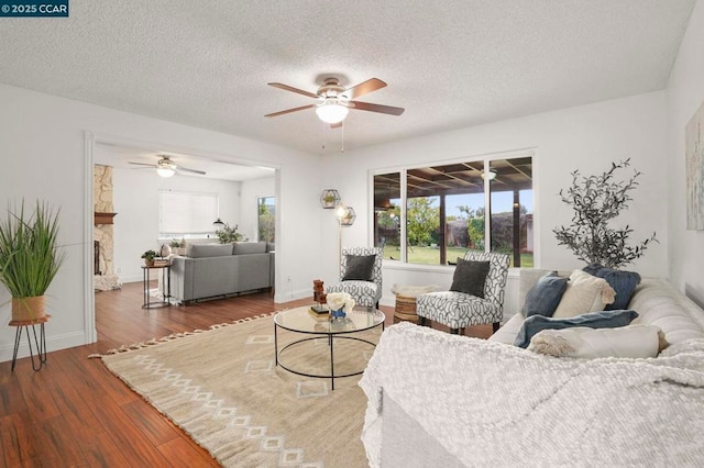 living room featuring ceiling fan, dark wood-type flooring, a fireplace, and a textured ceiling