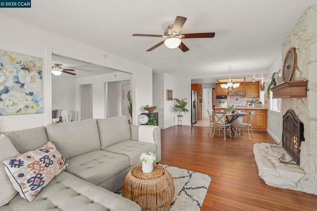 living room with ceiling fan with notable chandelier, a textured ceiling, and light hardwood / wood-style flooring