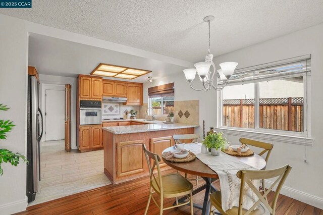 dining room with sink, a textured ceiling, a chandelier, and light hardwood / wood-style flooring