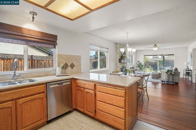 kitchen with sink, a healthy amount of sunlight, decorative light fixtures, stainless steel dishwasher, and kitchen peninsula