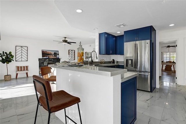 kitchen with sink, a kitchen bar, stainless steel refrigerator with ice dispenser, blue cabinets, and kitchen peninsula