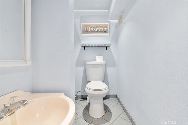 half bath with tile patterned flooring, a sink, toilet, and baseboards