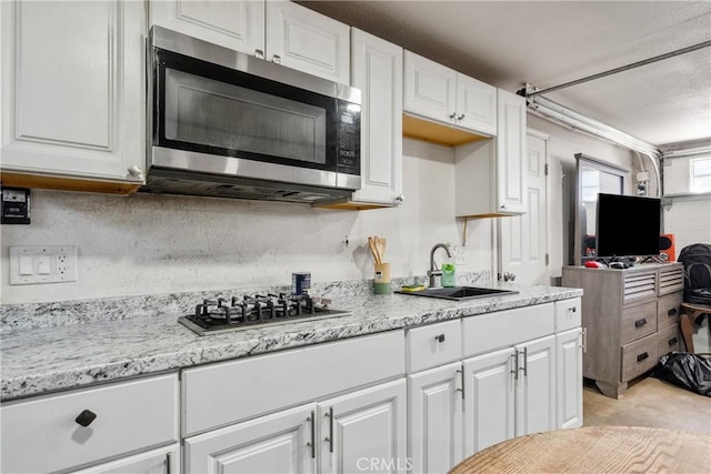 kitchen with light stone counters, stainless steel appliances, backsplash, white cabinetry, and a sink