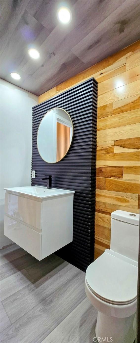 bathroom featuring wood walls, wood finished floors, vanity, toilet, and recessed lighting