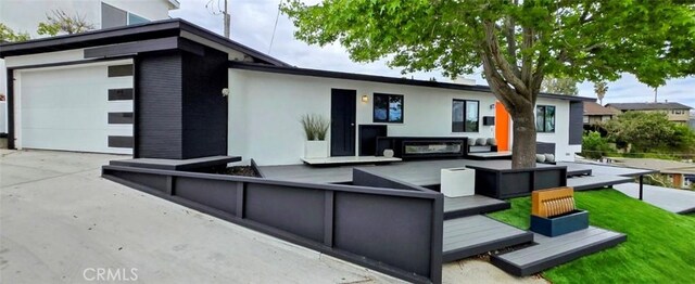 rear view of house featuring a garage, concrete driveway, stucco siding, and an outdoor living space