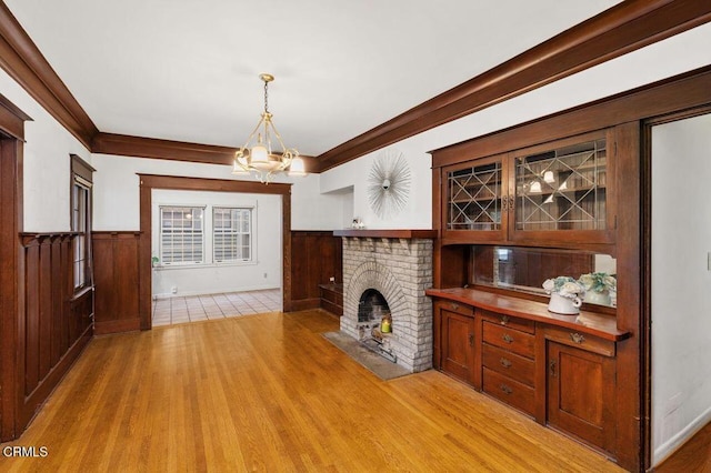 unfurnished living room with a brick fireplace, an inviting chandelier, and light hardwood / wood-style floors