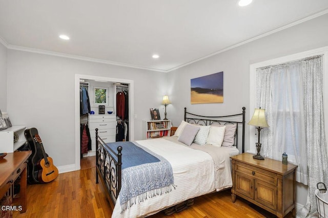 bedroom featuring a spacious closet, wood-type flooring, ornamental molding, and a closet