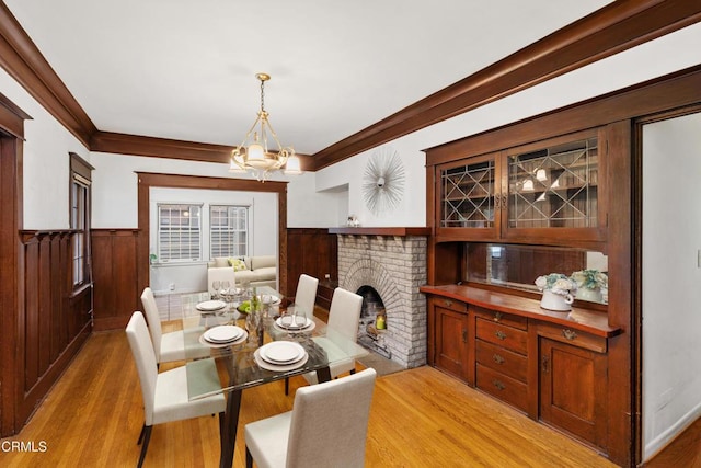 dining room with crown molding, a fireplace, an inviting chandelier, and light hardwood / wood-style floors