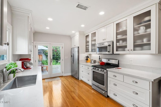 kitchen with appliances with stainless steel finishes, sink, light hardwood / wood-style flooring, white cabinets, and french doors