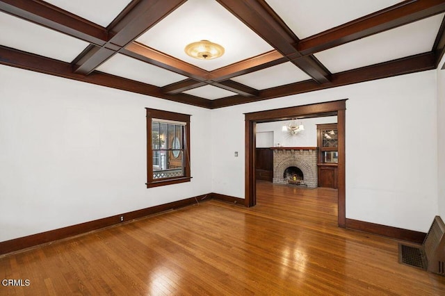 unfurnished living room featuring hardwood / wood-style flooring, coffered ceiling, a brick fireplace, and beamed ceiling