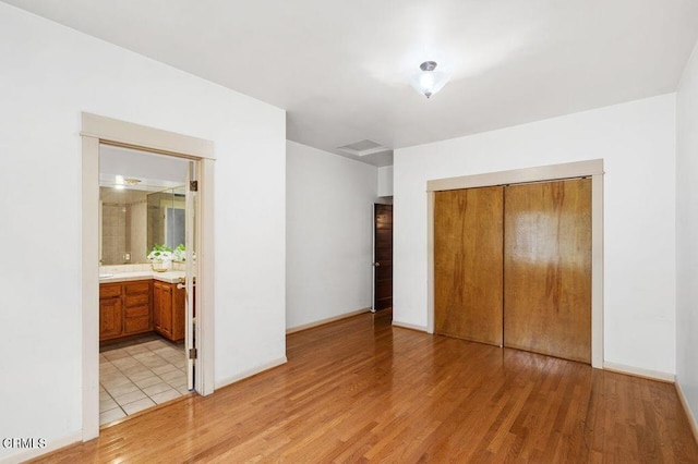 unfurnished bedroom featuring ensuite bathroom, a closet, and light wood-type flooring