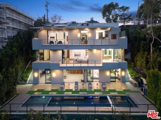 back house at dusk featuring a patio, a balcony, and a pool with hot tub