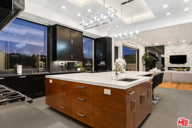 kitchen featuring a large fireplace, sink, a kitchen island with sink, and decorative light fixtures