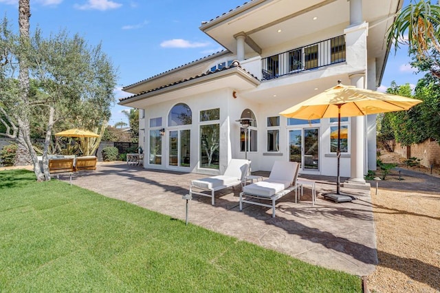 rear view of house featuring fence, a balcony, stucco siding, a patio area, and a lawn
