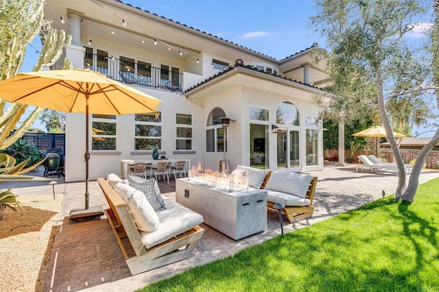 back of property featuring fence, a balcony, stucco siding, a patio area, and an outdoor living space with a fire pit