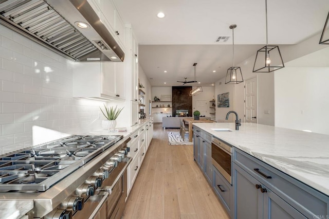 kitchen featuring white cabinets, cooktop, range hood, visible vents, and a sink
