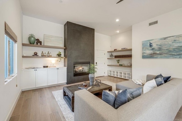 living room with light wood finished floors, baseboards, recessed lighting, visible vents, and a tile fireplace
