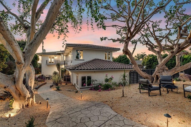 back of property at dusk with stucco siding, a tiled roof, and stairway
