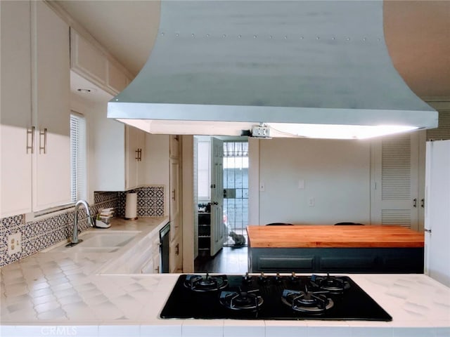 kitchen with sink, tasteful backsplash, island exhaust hood, black gas stovetop, and white cabinets