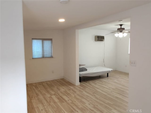 unfurnished bedroom featuring ceiling fan, a wall mounted AC, and light wood-type flooring